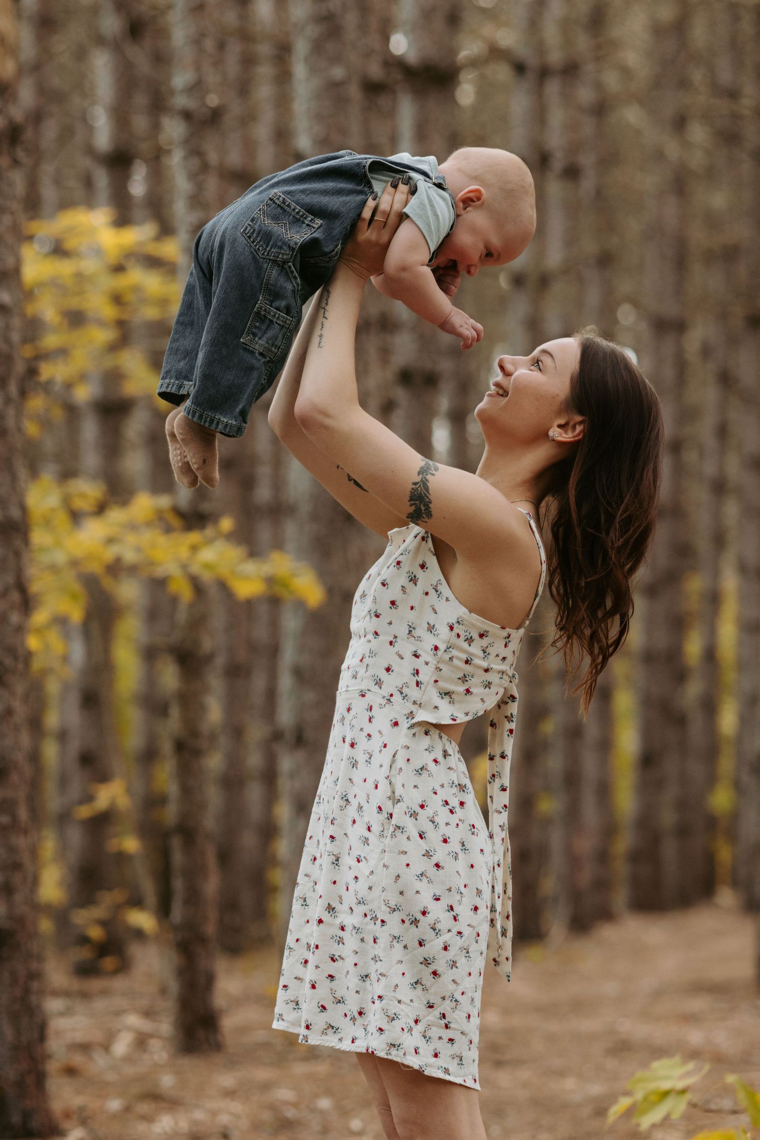 A sequence of four shots showing a person in a floral dress lifting and playing with a baby in a forest setting.