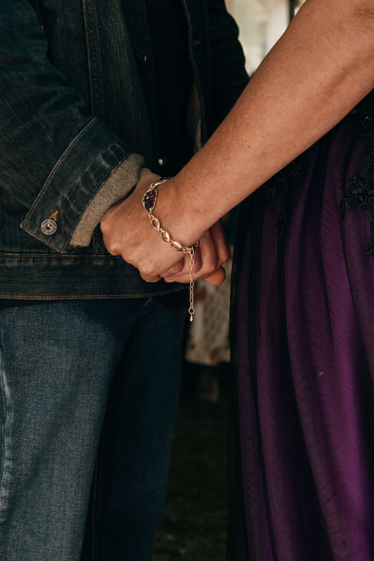 Close-up of two people holding hands while wearing handcuffs, with denim jacket and purple dress visible.