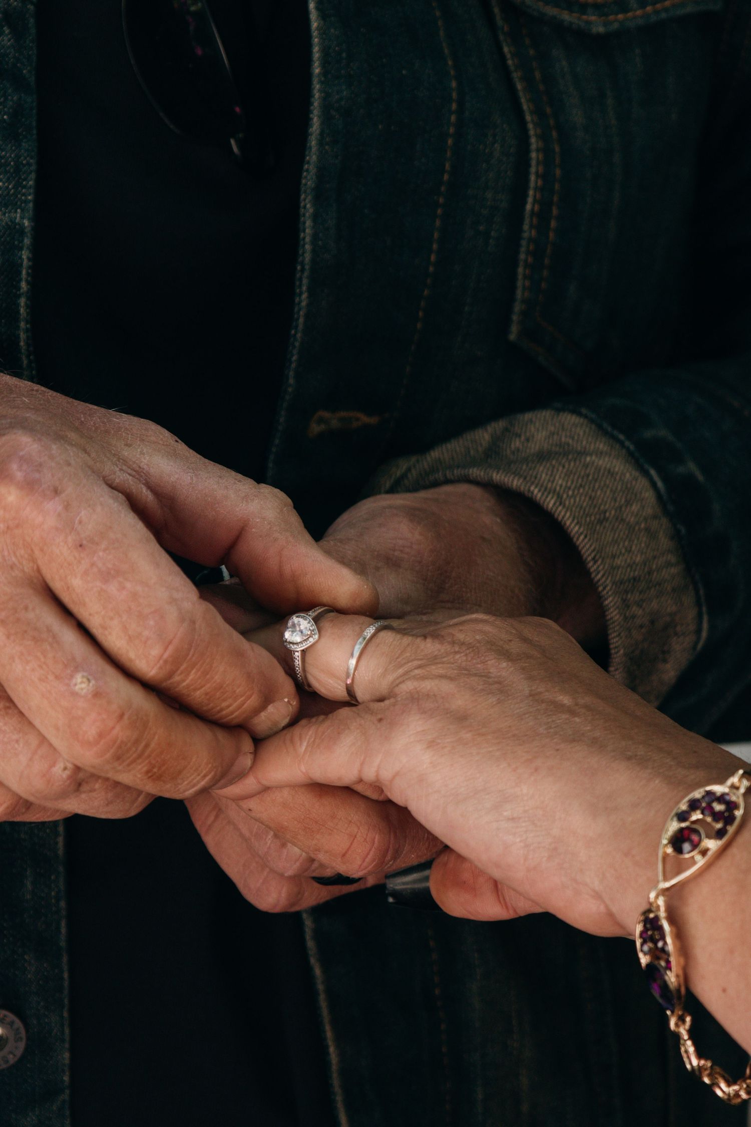 Close up of hands putting on an engagement ring with a diamond solitaire during a proposal moment.