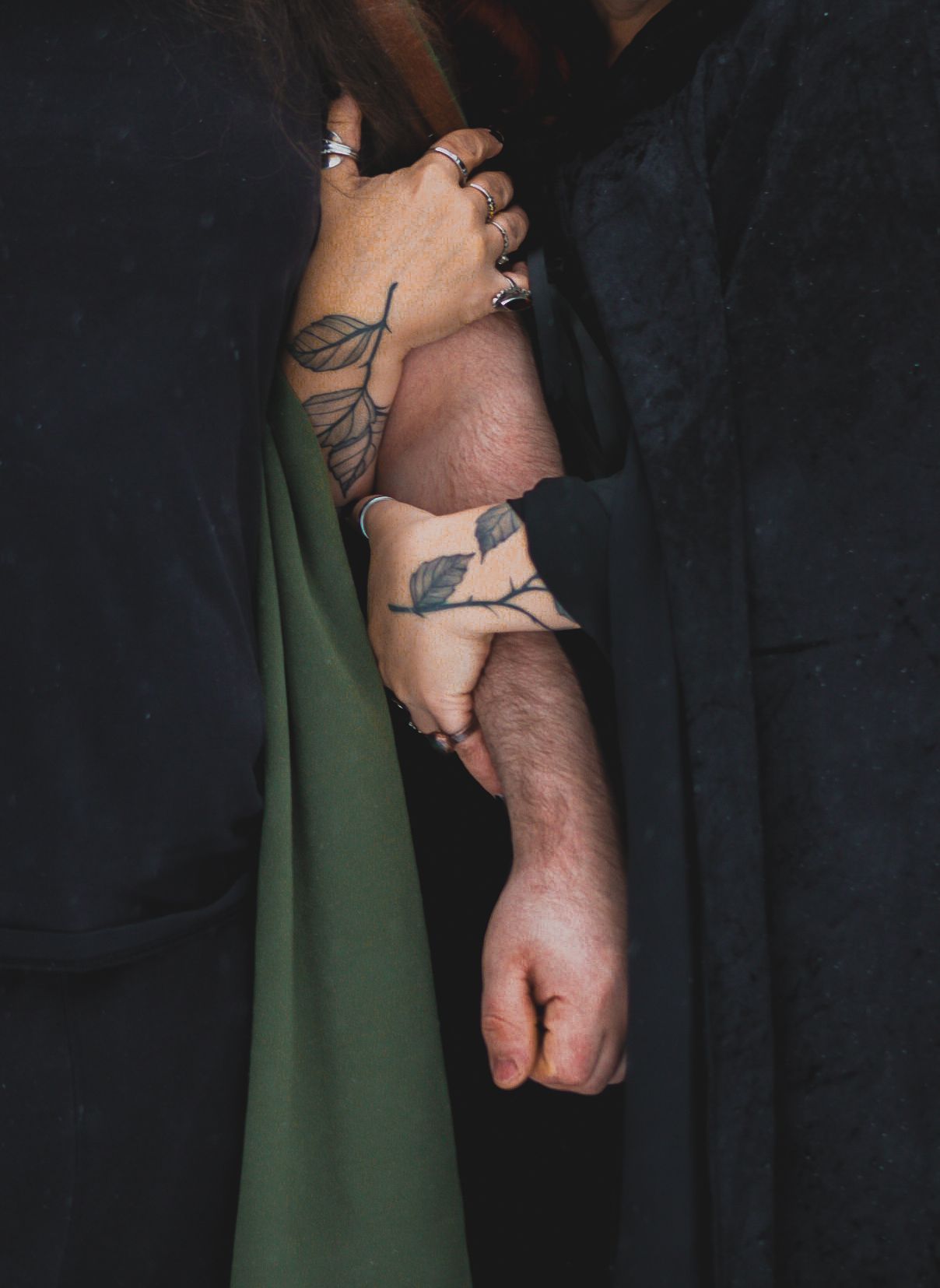 A close-up photo of a hand with tattoos against a dark black background with a green fabric draping down.