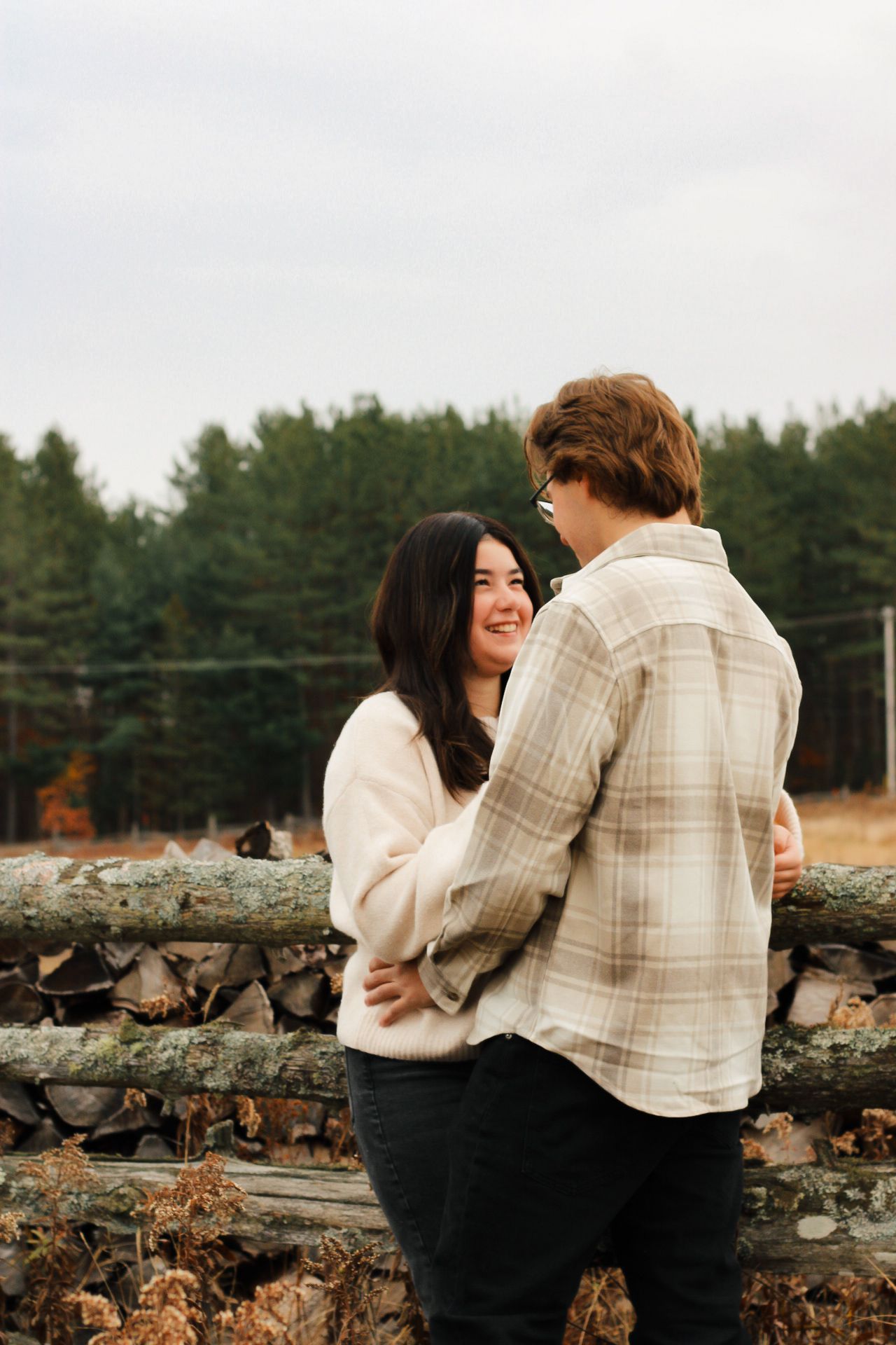 Couple embracing by rustic wooden fence in rural winter setting.