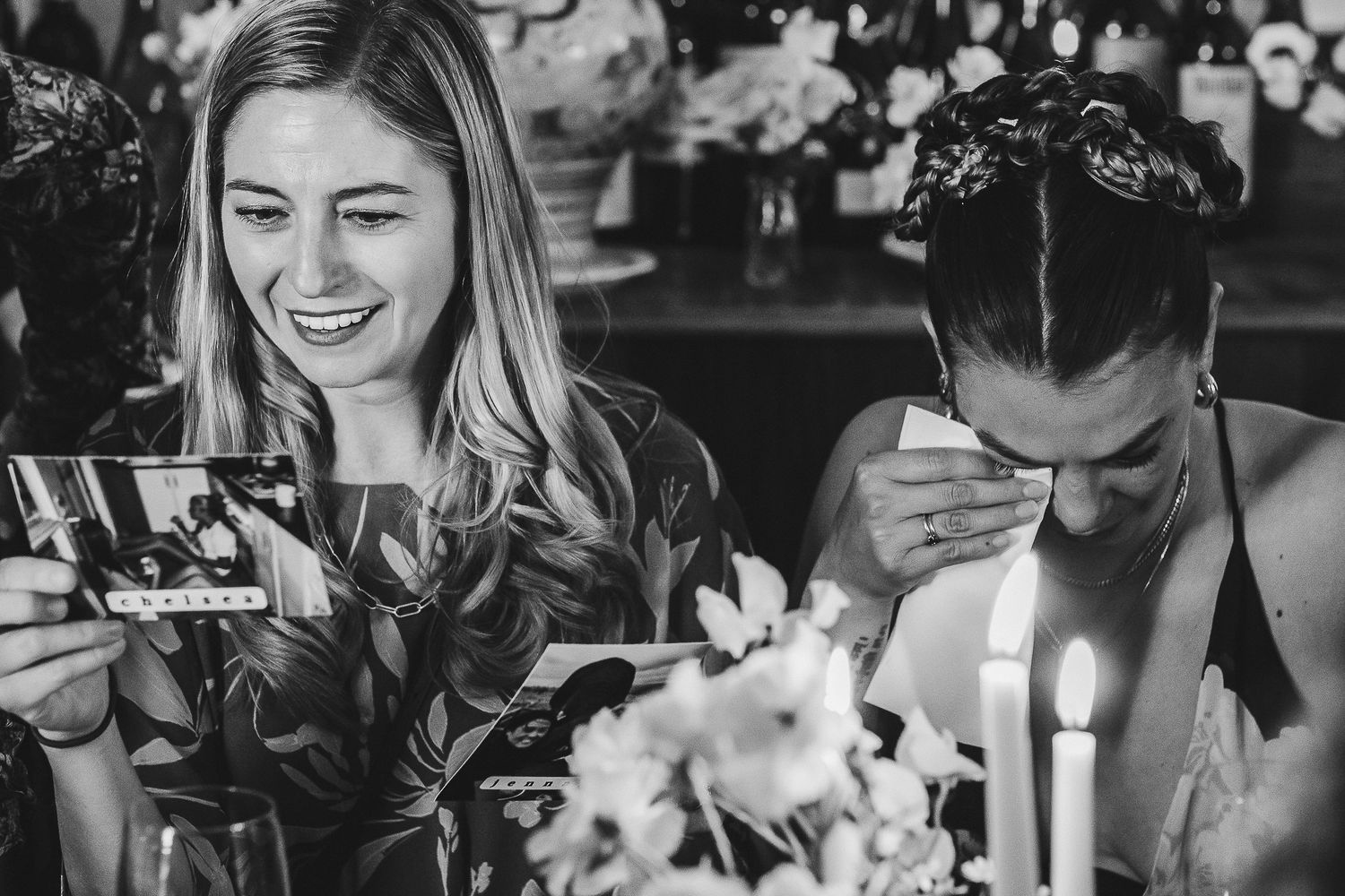 Black and white photo of a couple looking at photos while sitting at a table with flowers and candles.