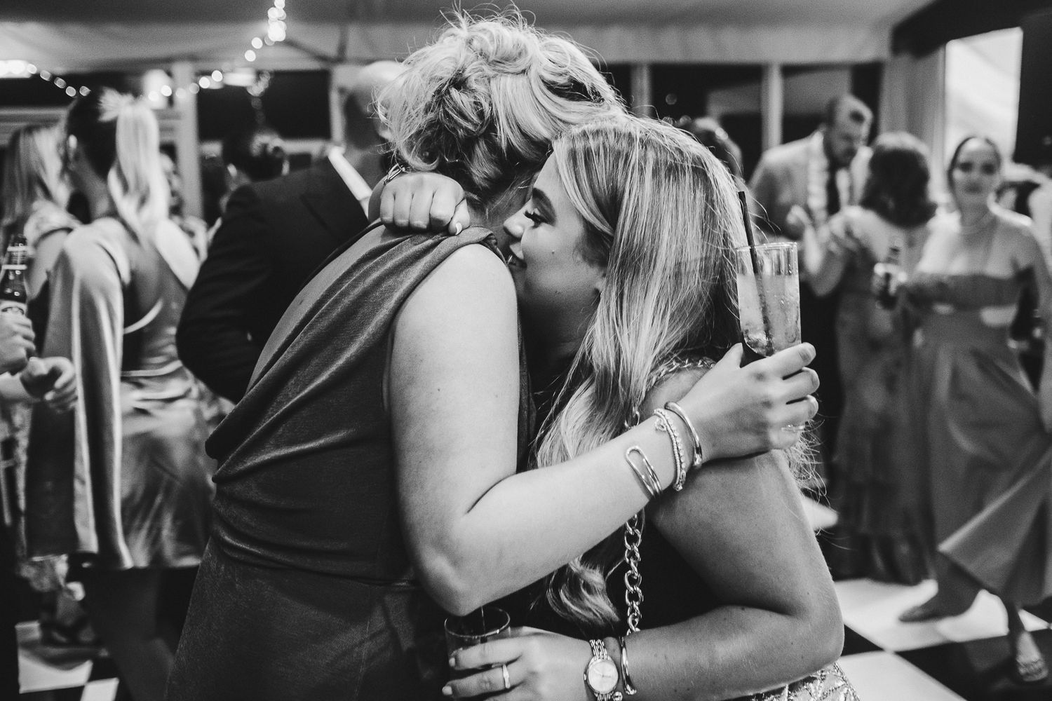 A tender moment captured in black and white as two figures embrace emotionally during what appears to be a celebration.