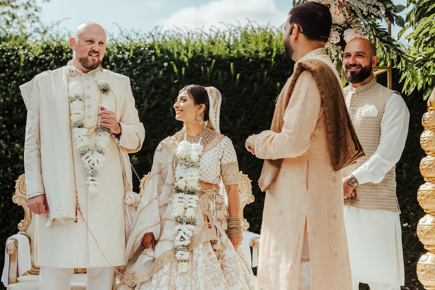 Traditional South Asian wedding ceremony with participants wearing elegant cream and white traditional attire outdoors.