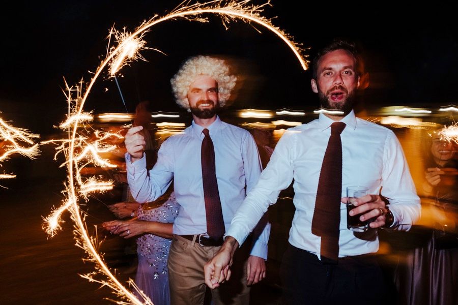 Two wedding guests pose with sparklers creating a light trail in the nighttime.