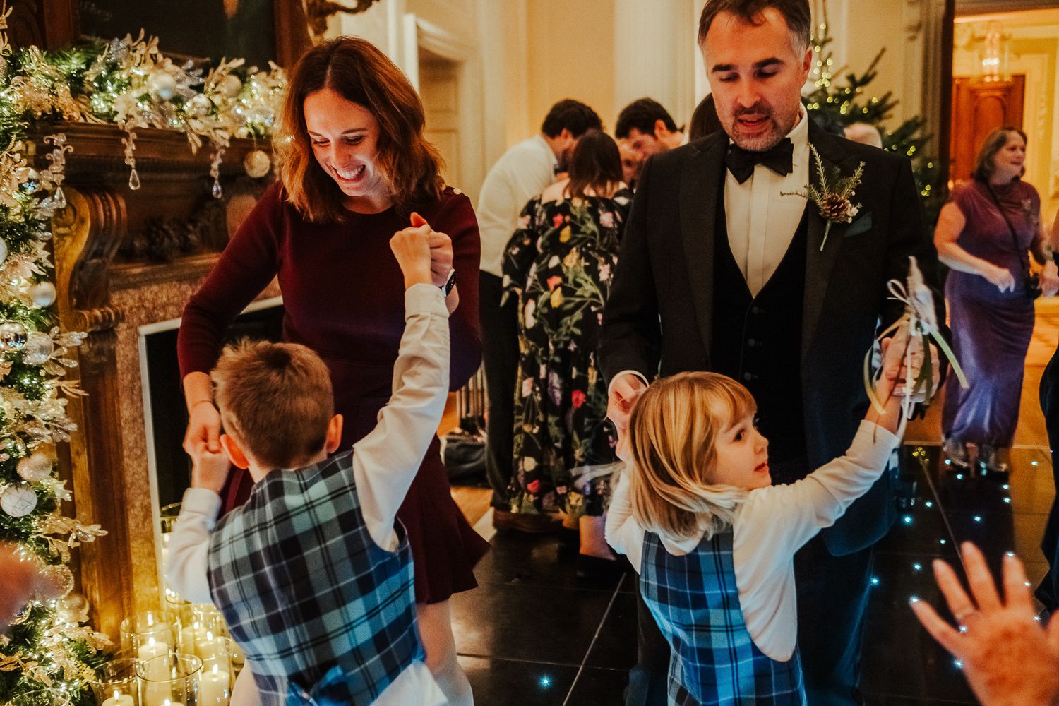 Wedding party celebrates with enthusiastic dancing and raised arms in a decorated reception venue.