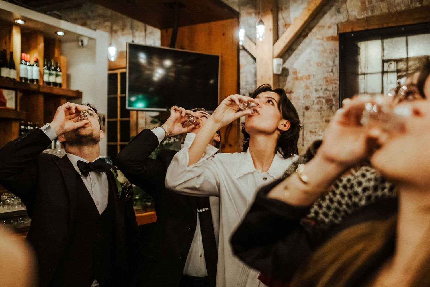Wedding party takes celebratory shots together at rustic venue bar.