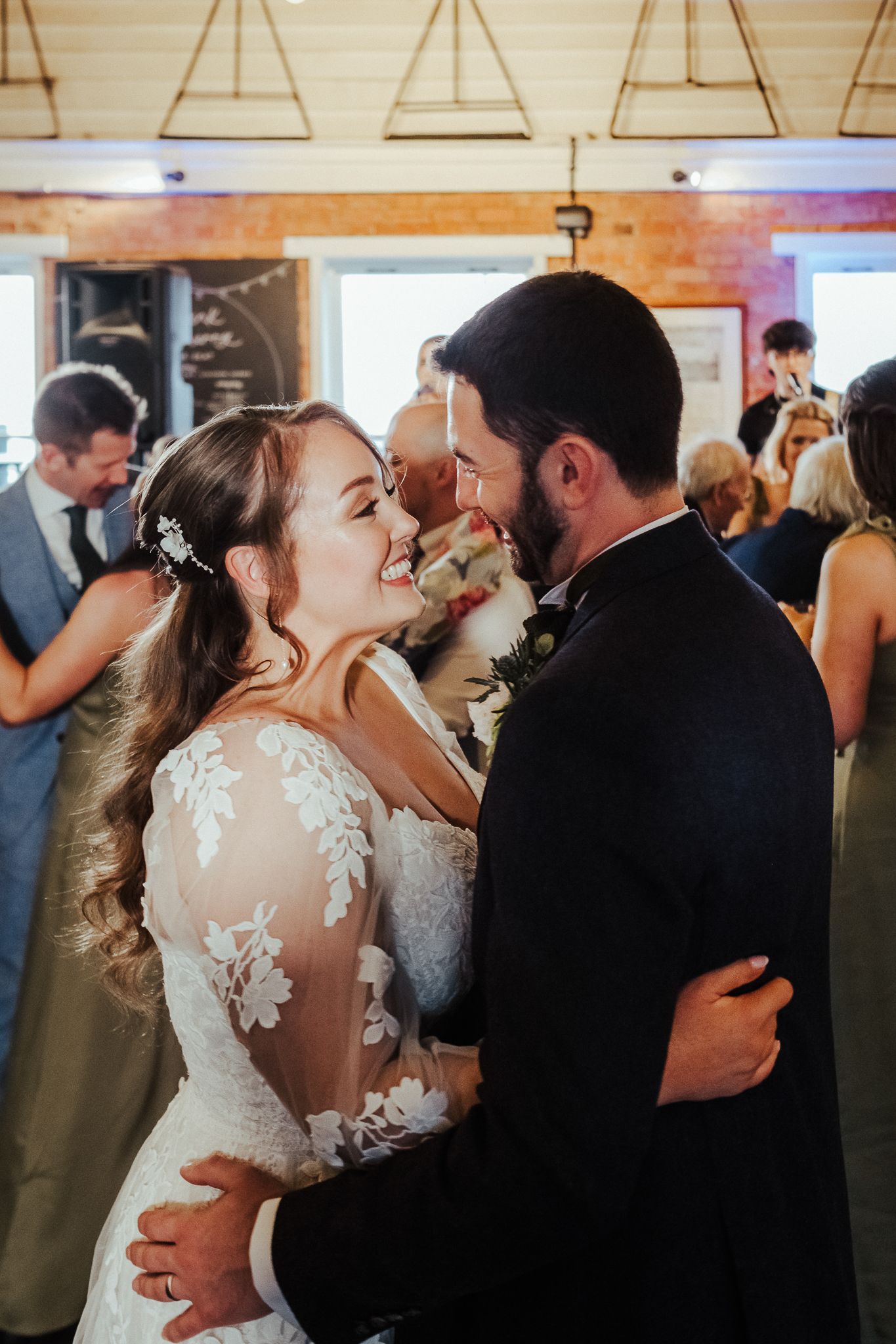 A joyful wedding couple shares a romantic dance together in a rustic venue with string lights overhead.