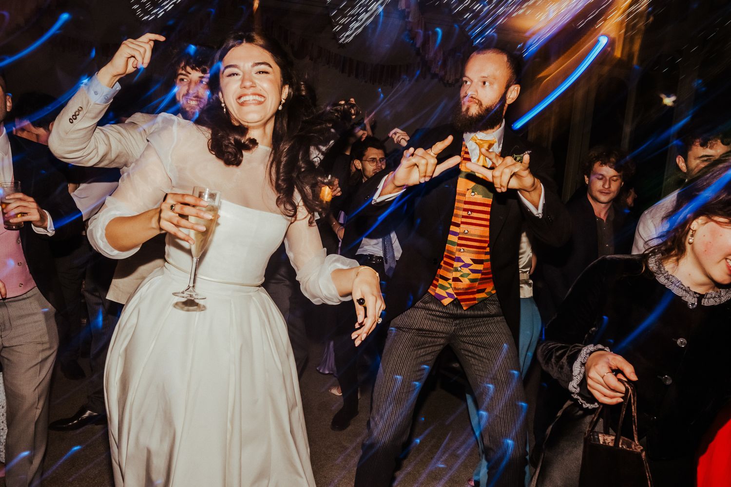People dancing and celebrating with drinks at a lively wedding reception party.