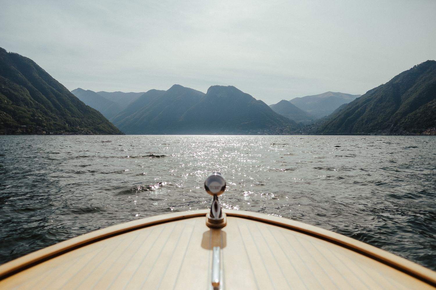 Wooden boat bow cutting through lake waters with dramatic mountain vista.