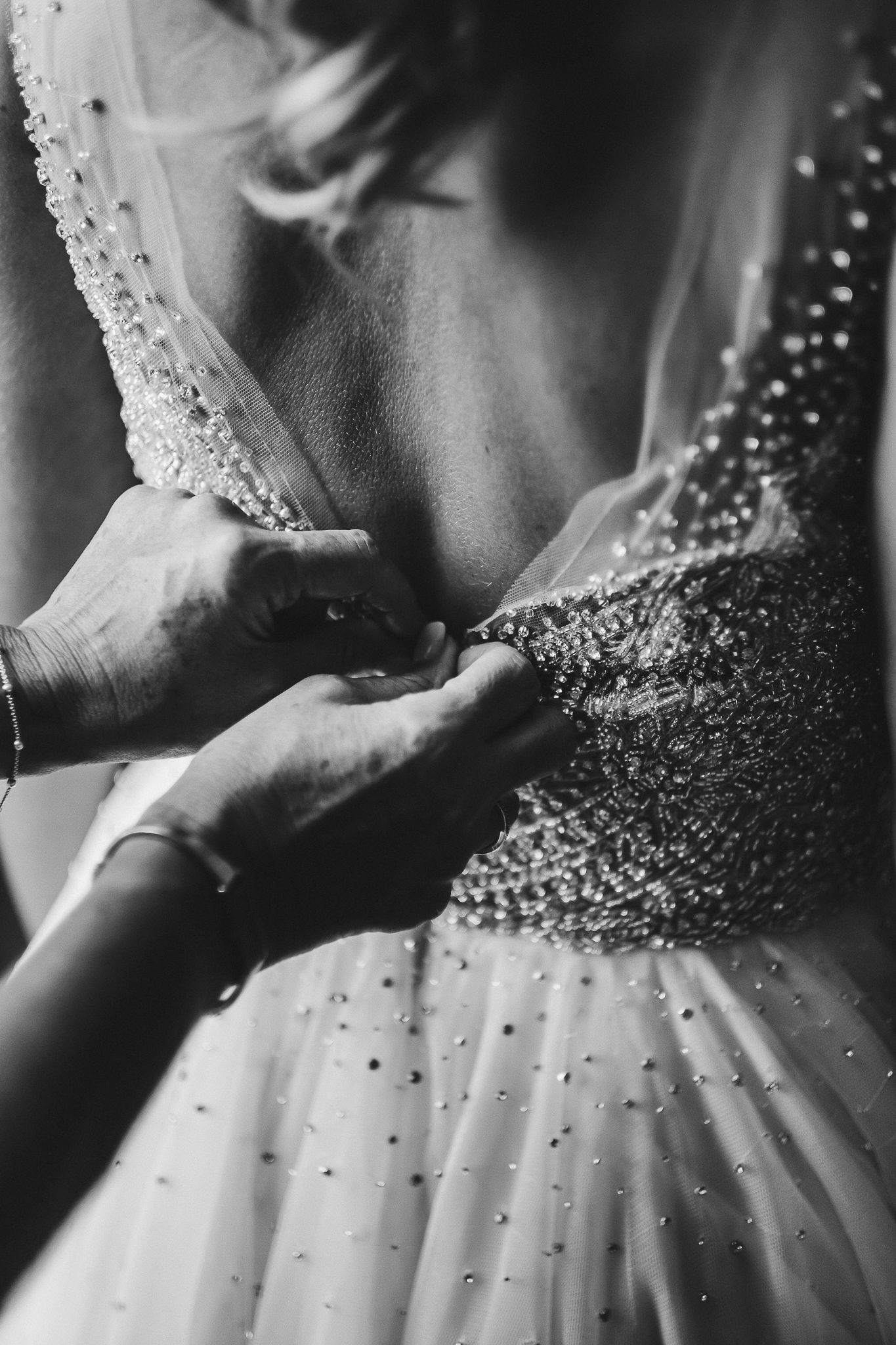 Black and white detail shot of hands adjusting sparkly beaded wedding dress.