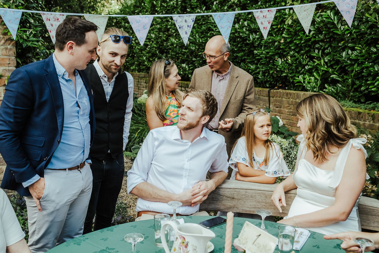 Wedding guests socialize under white bunting decorations at casual outdoor reception.