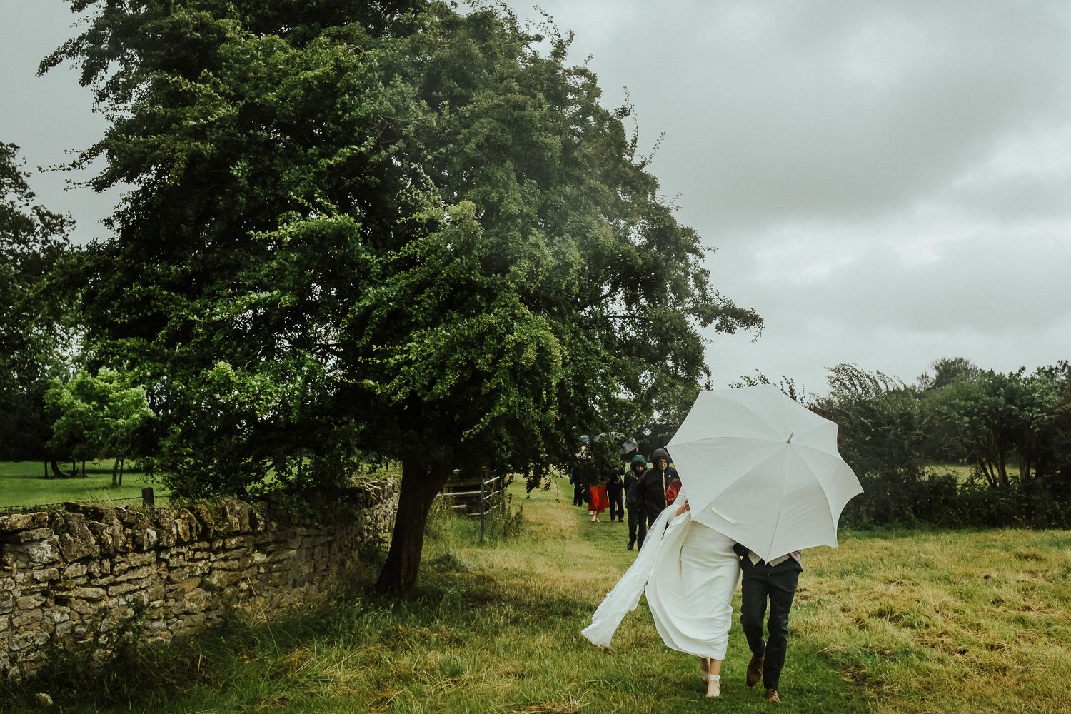 Overcast wedding day with trees and stone walls creating a romantic countryside atmosphere.