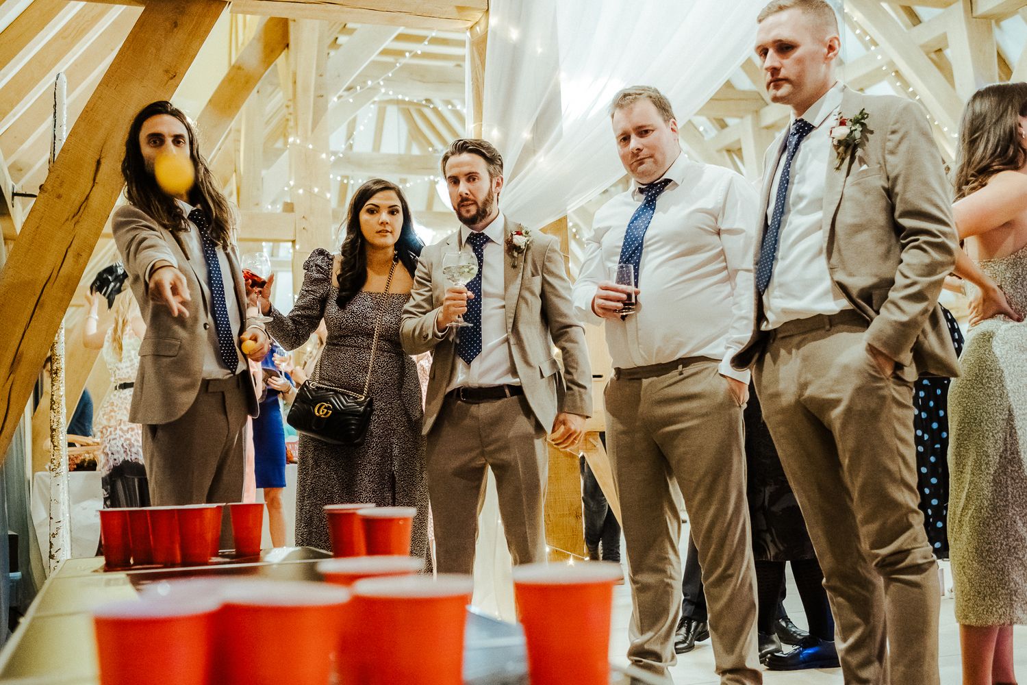 Wedding guests playing beer pong at a rustic barn reception.