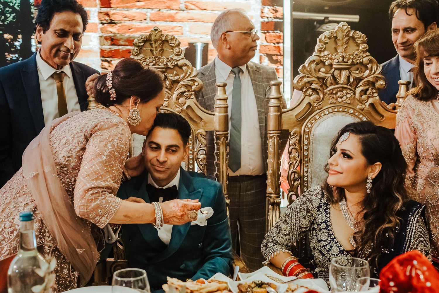 Guests celebrate around ornate throne chairs at wedding reception dinner.
