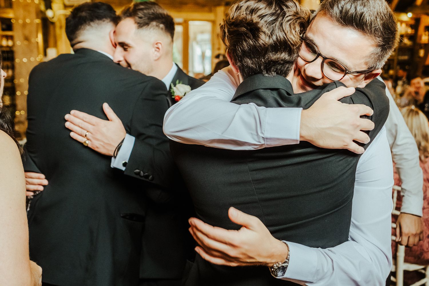 A joyful wedding party embraces and celebrates during an indoor reception.
