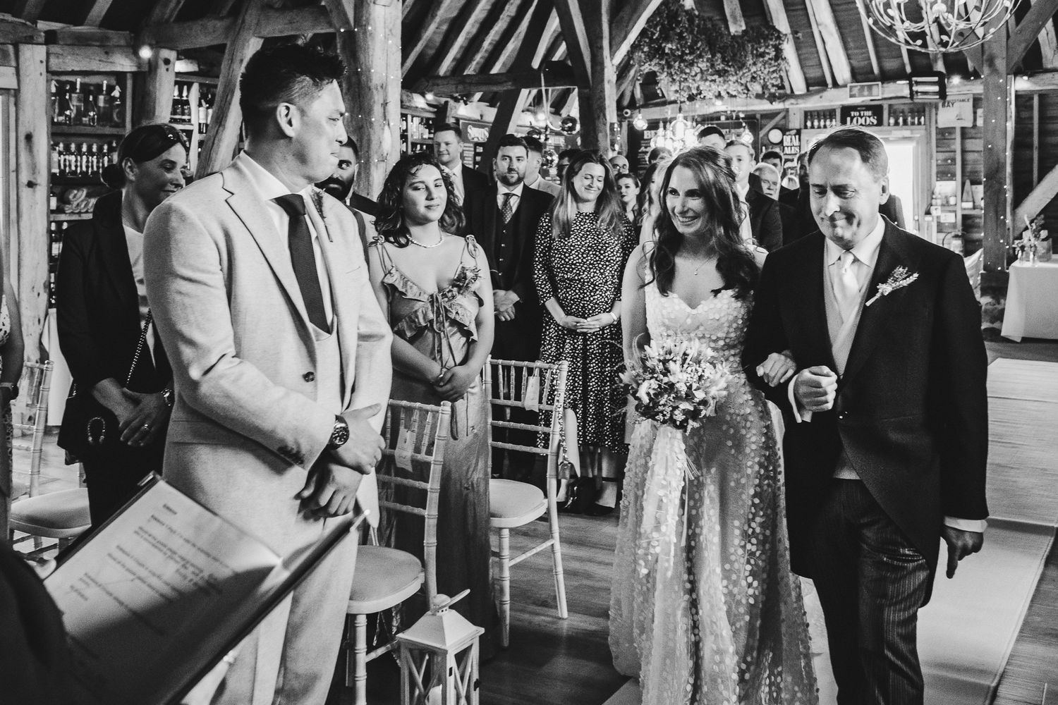 Black and white candid photo of wedding ceremony reactions in rustic venue.