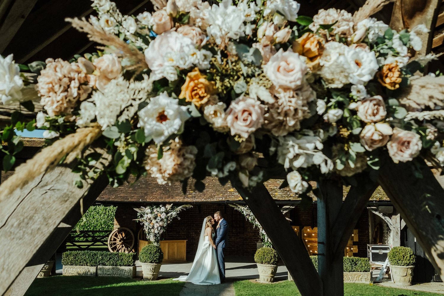 Ornate floral arch with white and peach blooms frames wedding couple beneath.