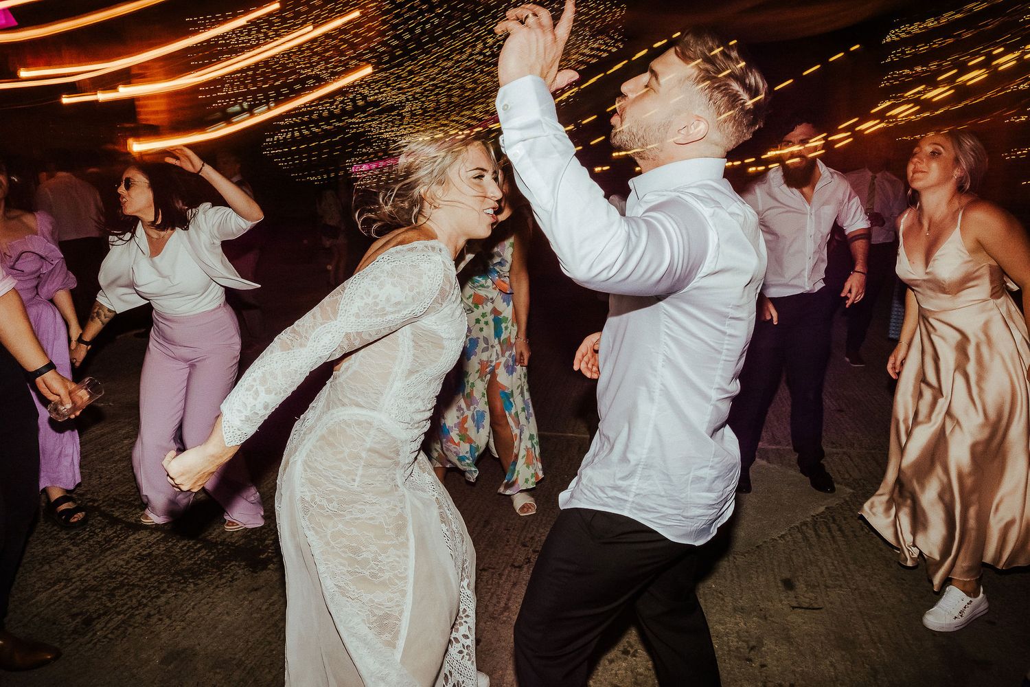Wedding guests show off their energetic dance moves under decorative string lights at the reception.
