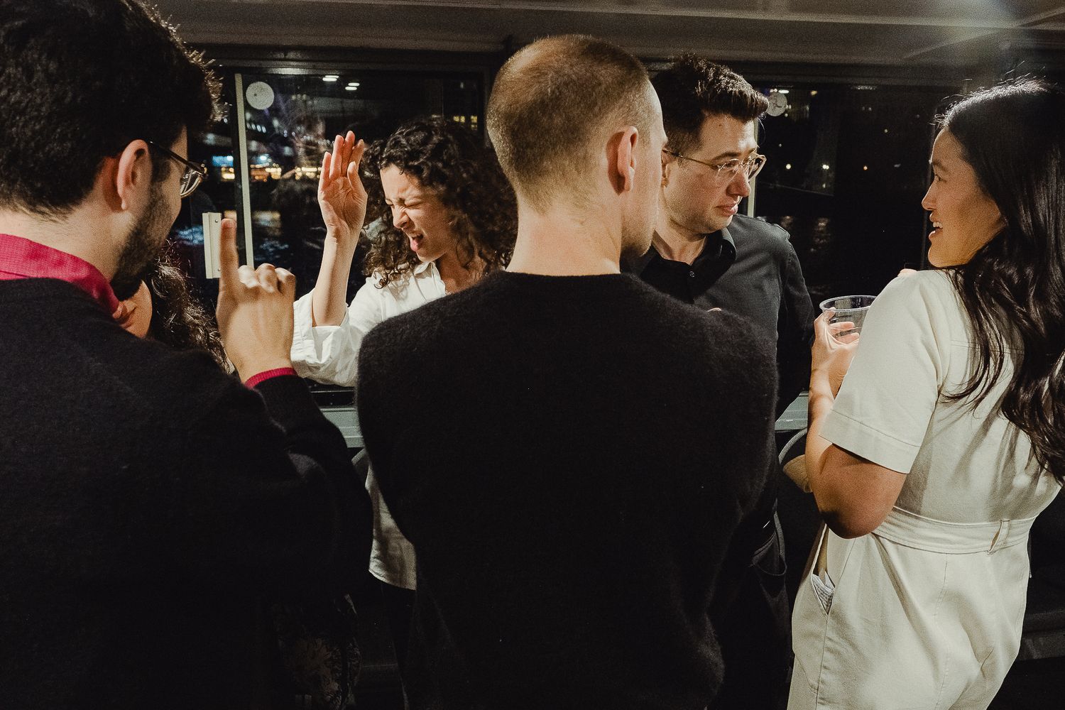 A group of people gather in conversation at a dimly lit bar or social venue during a nighttime event.