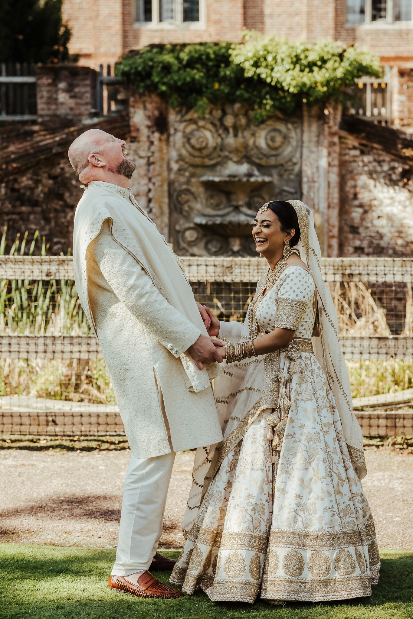 A couple shares a joyful moment in their wedding attire at an elegant garden setting with historic architecture.