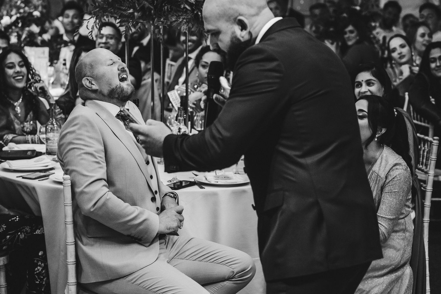 Two people share an emotional moment during a formal dinner event, captured in black and white photography.