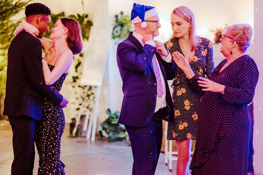 Multiple couples dancing and socializing at a festive indoor celebration with colorful lighting.