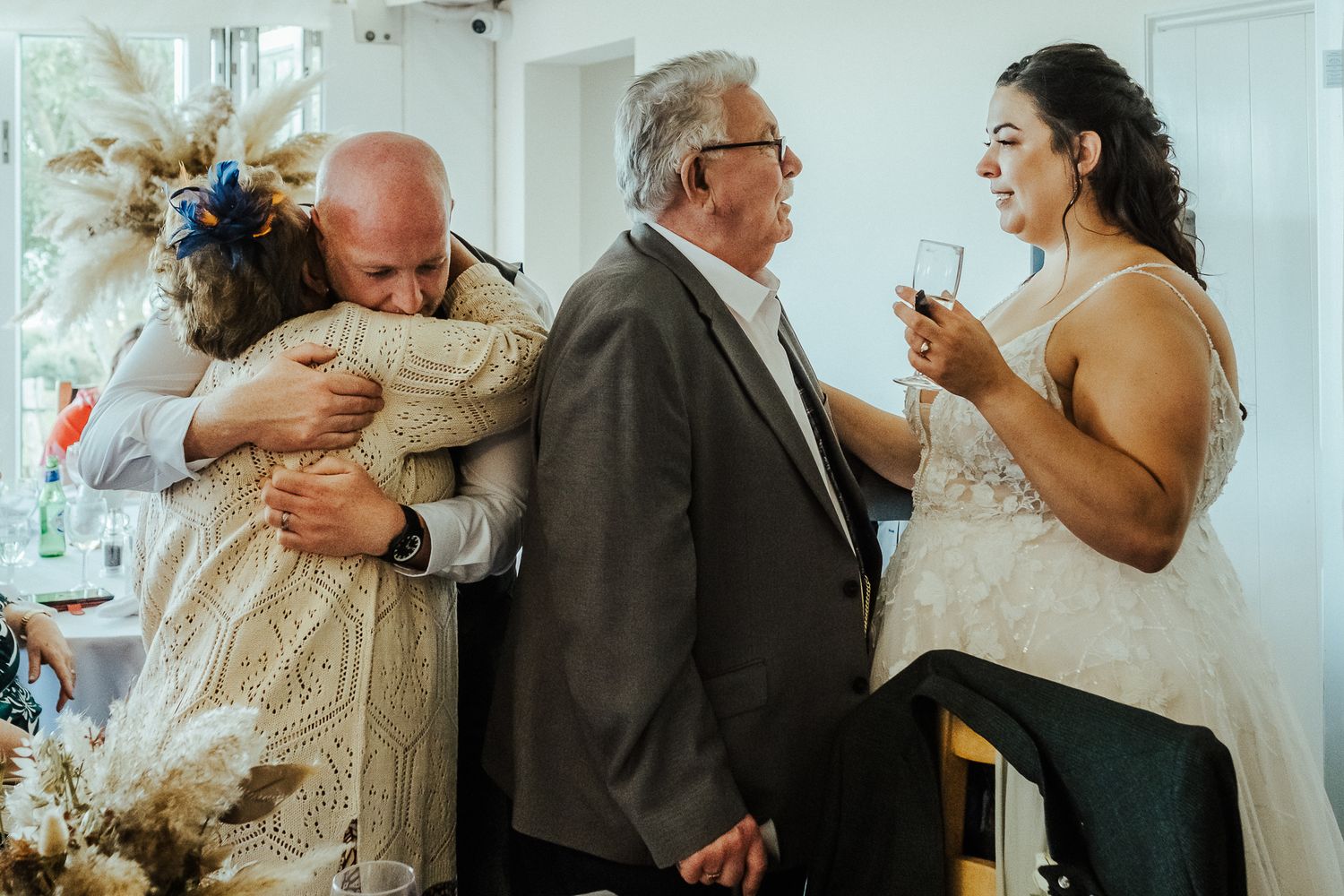 Emotional wedding reception scene with guests sharing hugs and conversations in a bright indoor space.