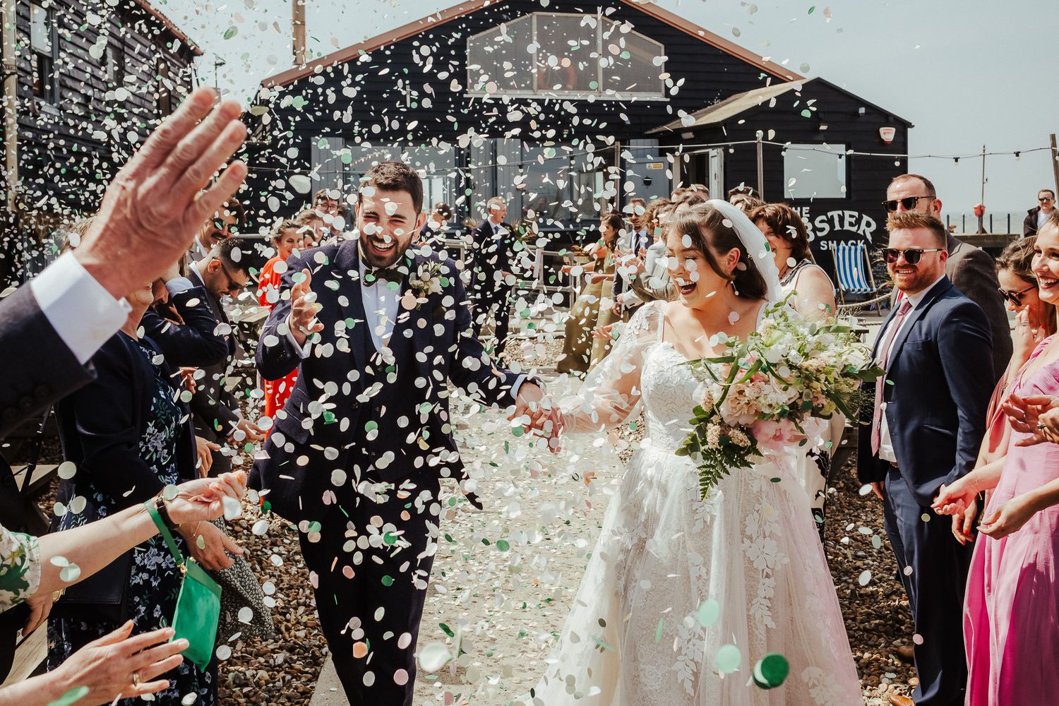 A joyful wedding exit with guests throwing confetti outside a rustic venue.