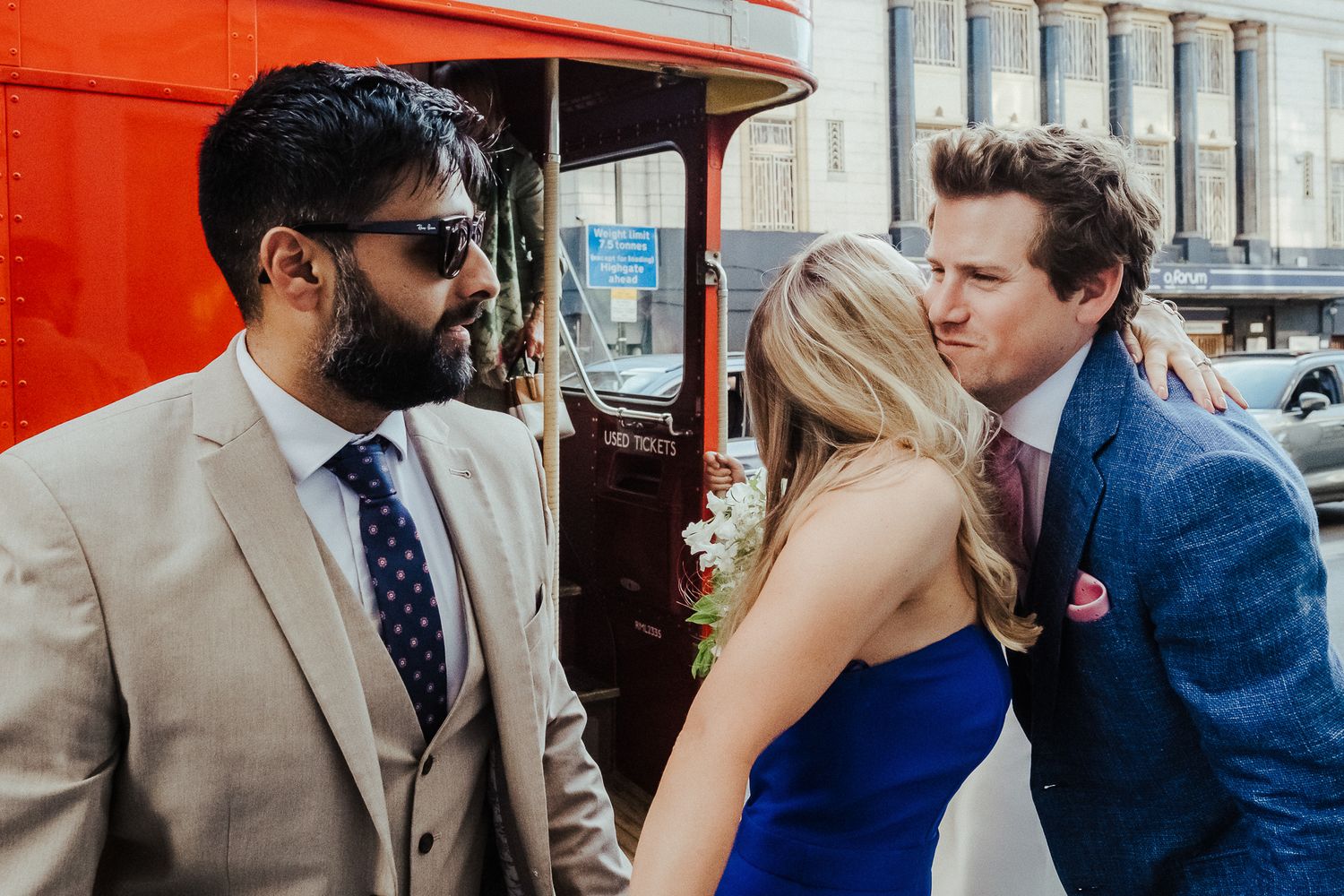 A group gathered around a red vintage bus entrance during a wedding celebration.