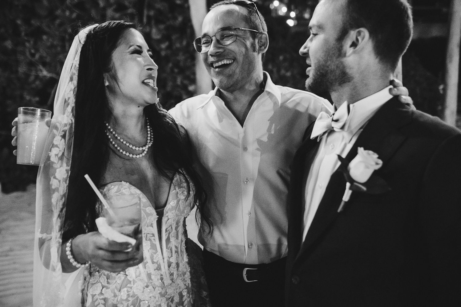 Three guests share laughter during a festive wedding celebration.