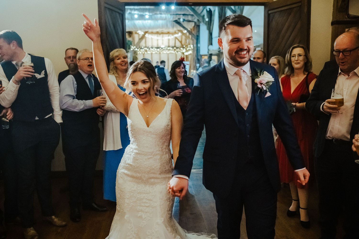 A joyful couple makes their grand entrance at their wedding reception while guests look on and celebrate.