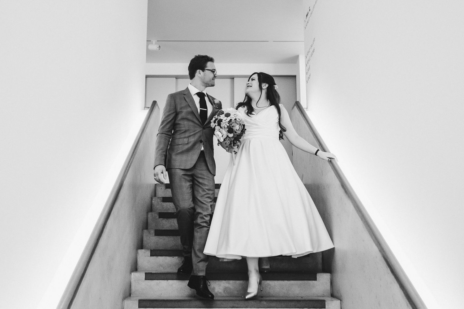 A couple in wedding attire poses on stairs at their vintage-inspired wedding celebration.