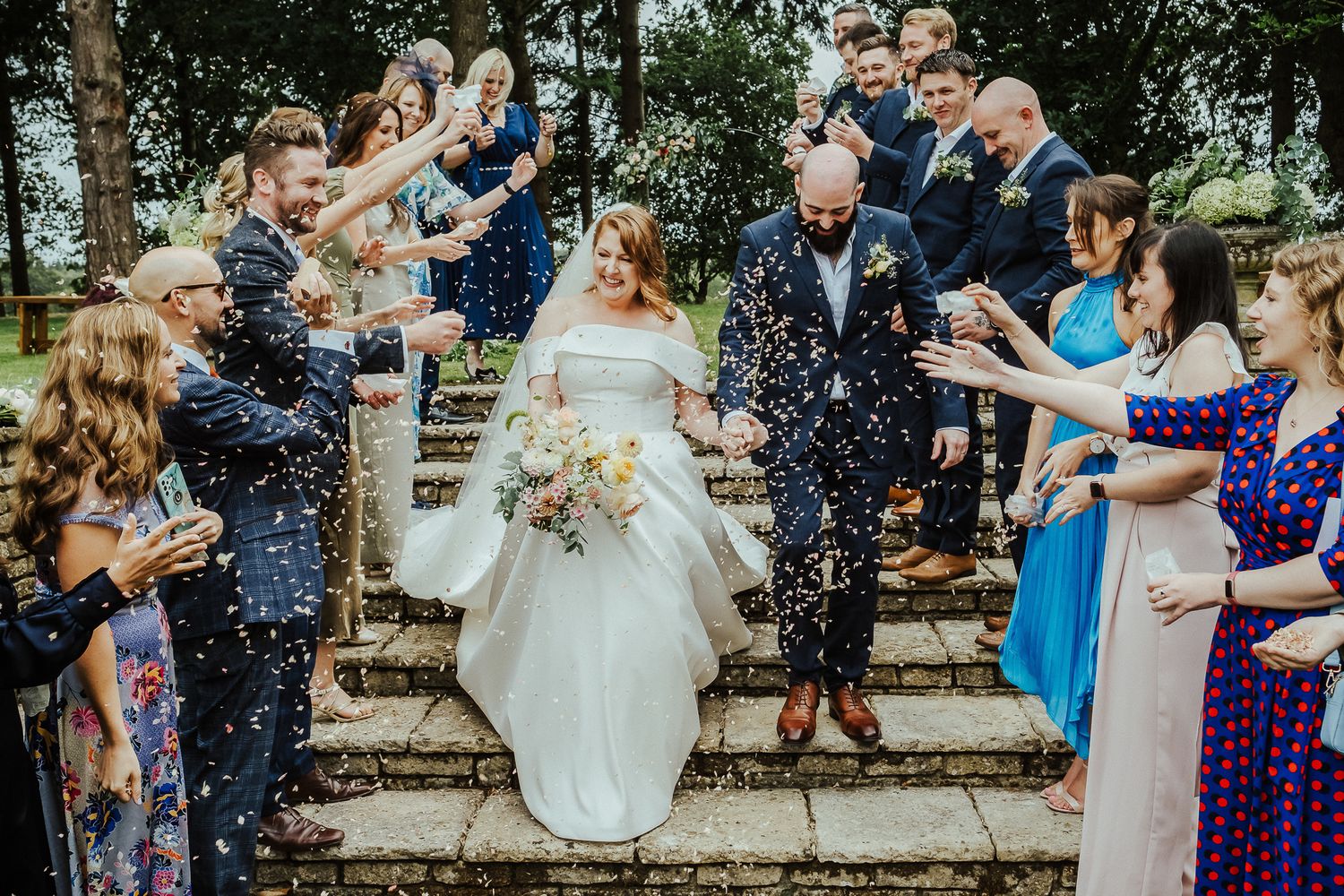 Wedding guests shower the newlyweds with confetti as they descend stone steps together.