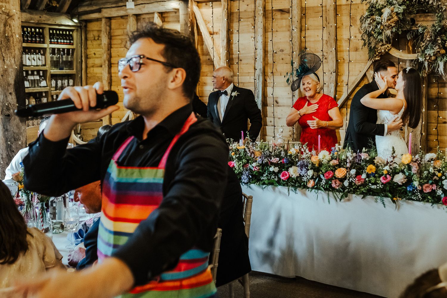 Wedding reception guests enjoying drinks and conversation in a rustic wood-paneled venue with decorative floral arrangements.