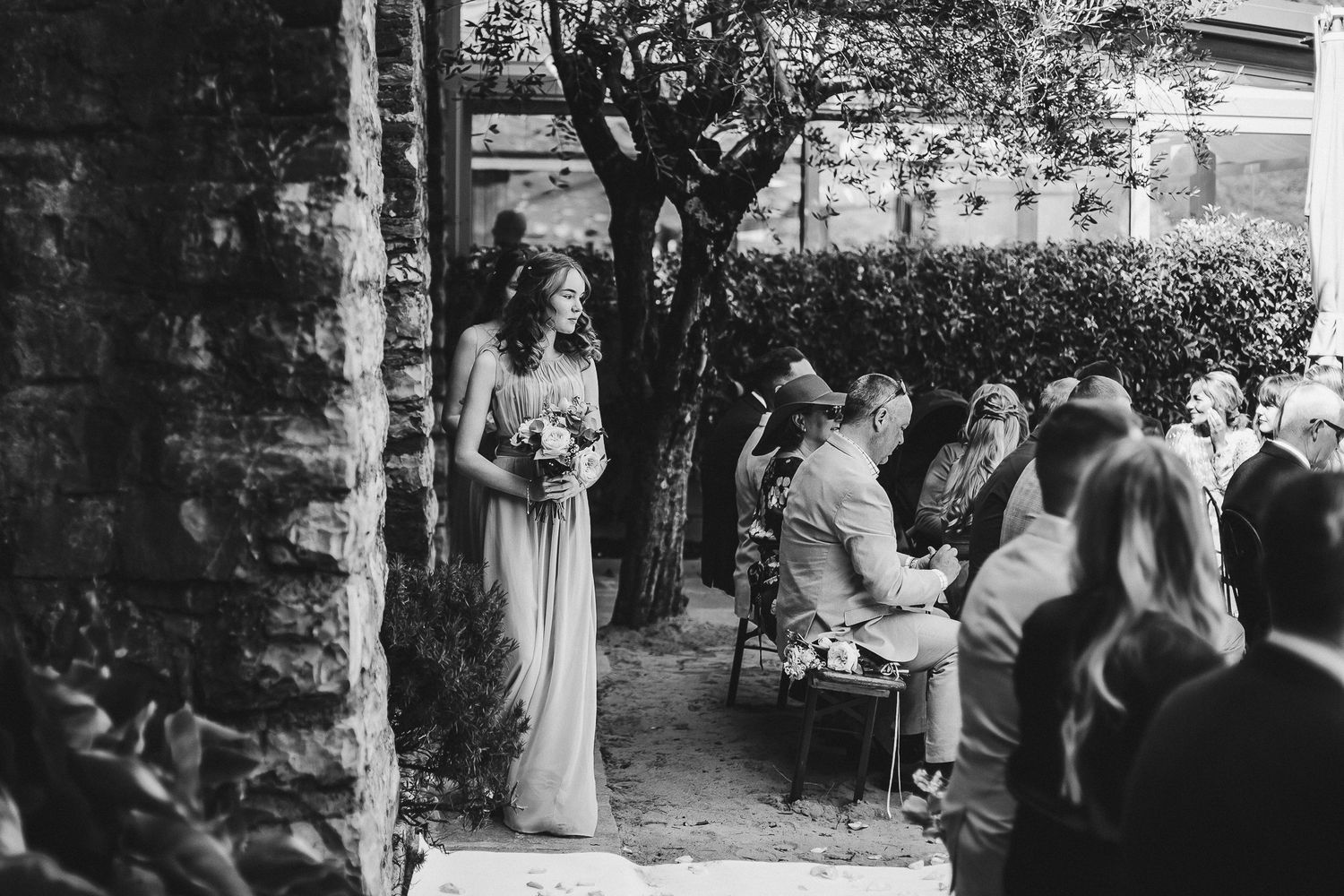 Black and white candid shot of outdoor garden wedding ceremony with guests seated.