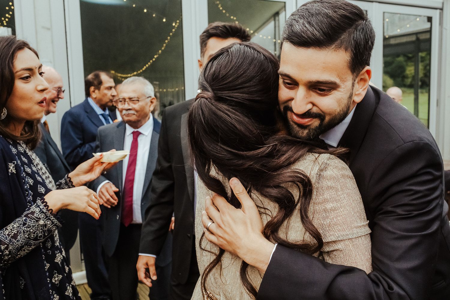 Heartfelt embraces and joyful reactions during an emotional wedding celebration with guests gathered around.