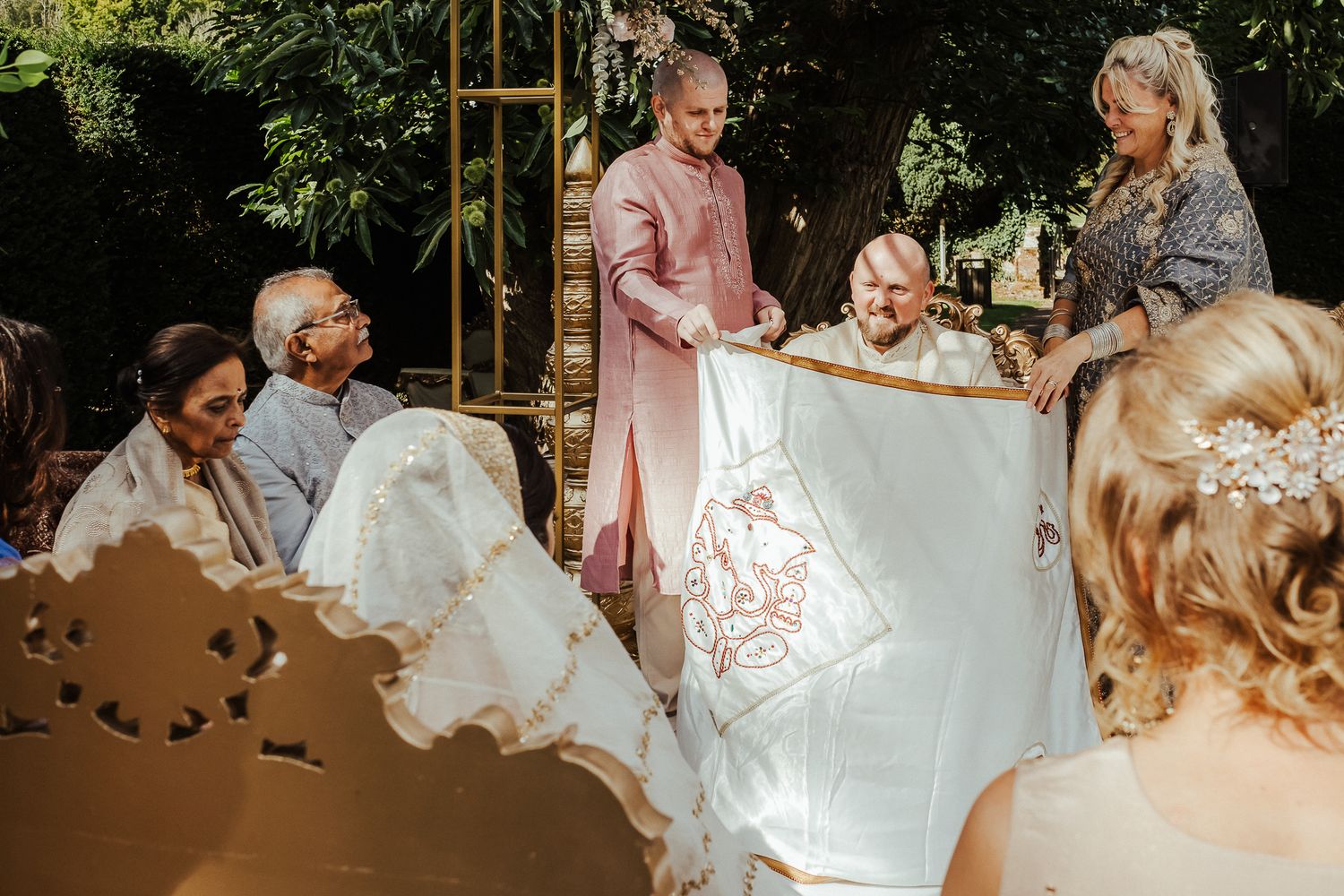 A group of people gather outdoors during a sunny celebration event, with elegant decor visible in the background.