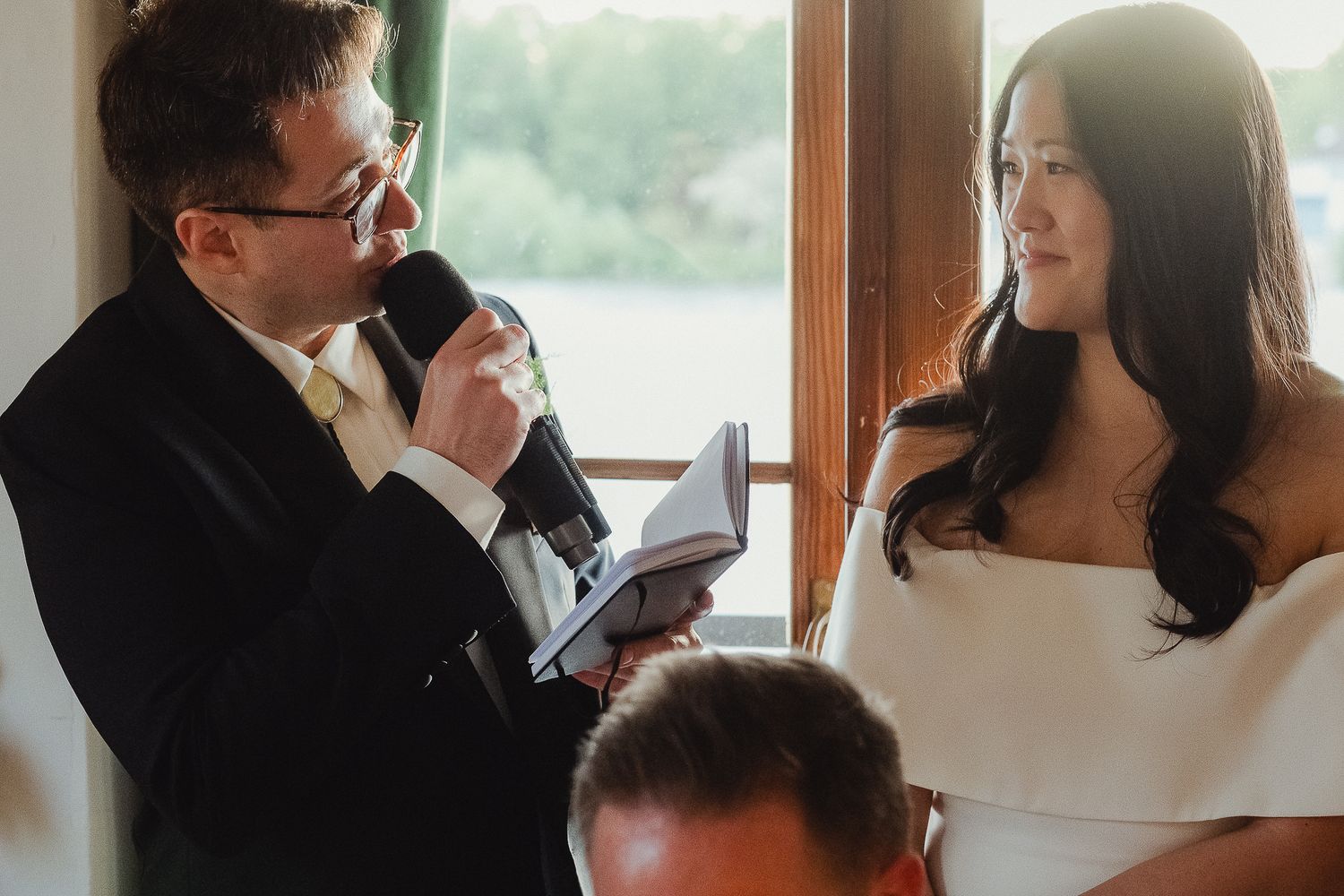 Wedding guest delivers emotional speech at reception while others smile and listen attentively.