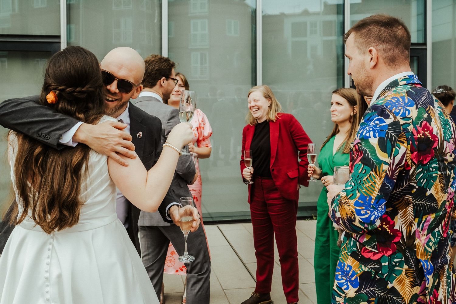 Wedding guests mingling and embracing at a modern venue with glass walls.