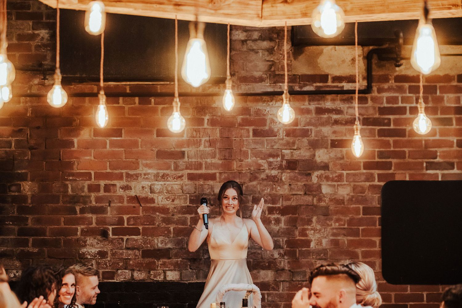A celebration in a rustic brick venue with hanging Edison bulbs creates a warm atmosphere.