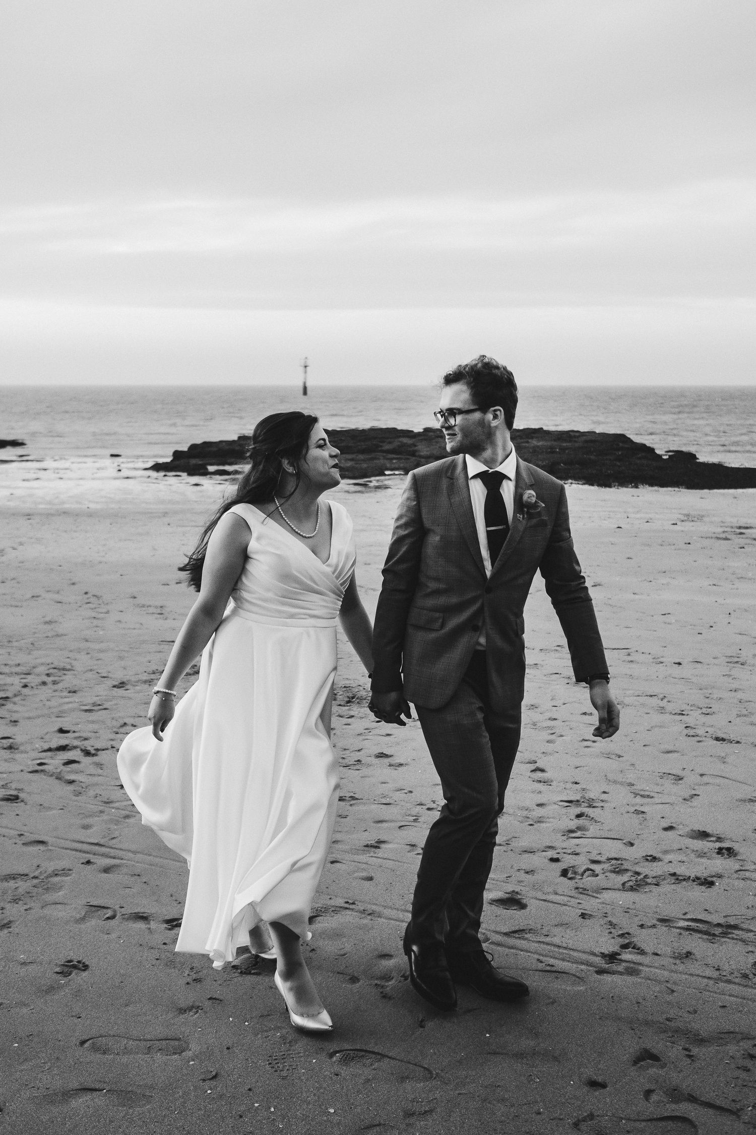 Black and white photo of a couple strolling together on a sandy beach.