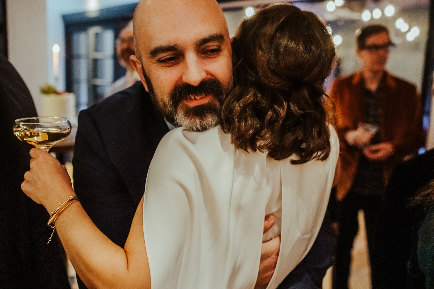A candid reception moment shows guests celebrating with drinks and hugs.