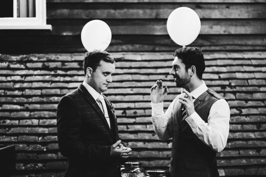 Black and white photo of groomsmen posing with white balloons against wooden wall.