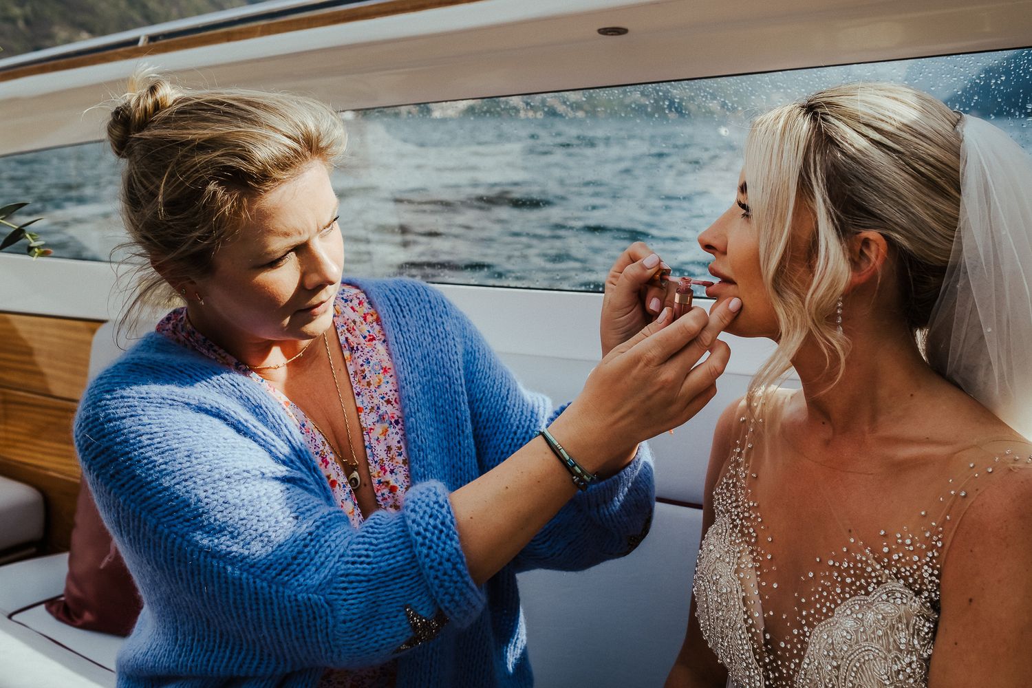 A final touch up of wedding makeup being applied on a boat against a waterfront background.