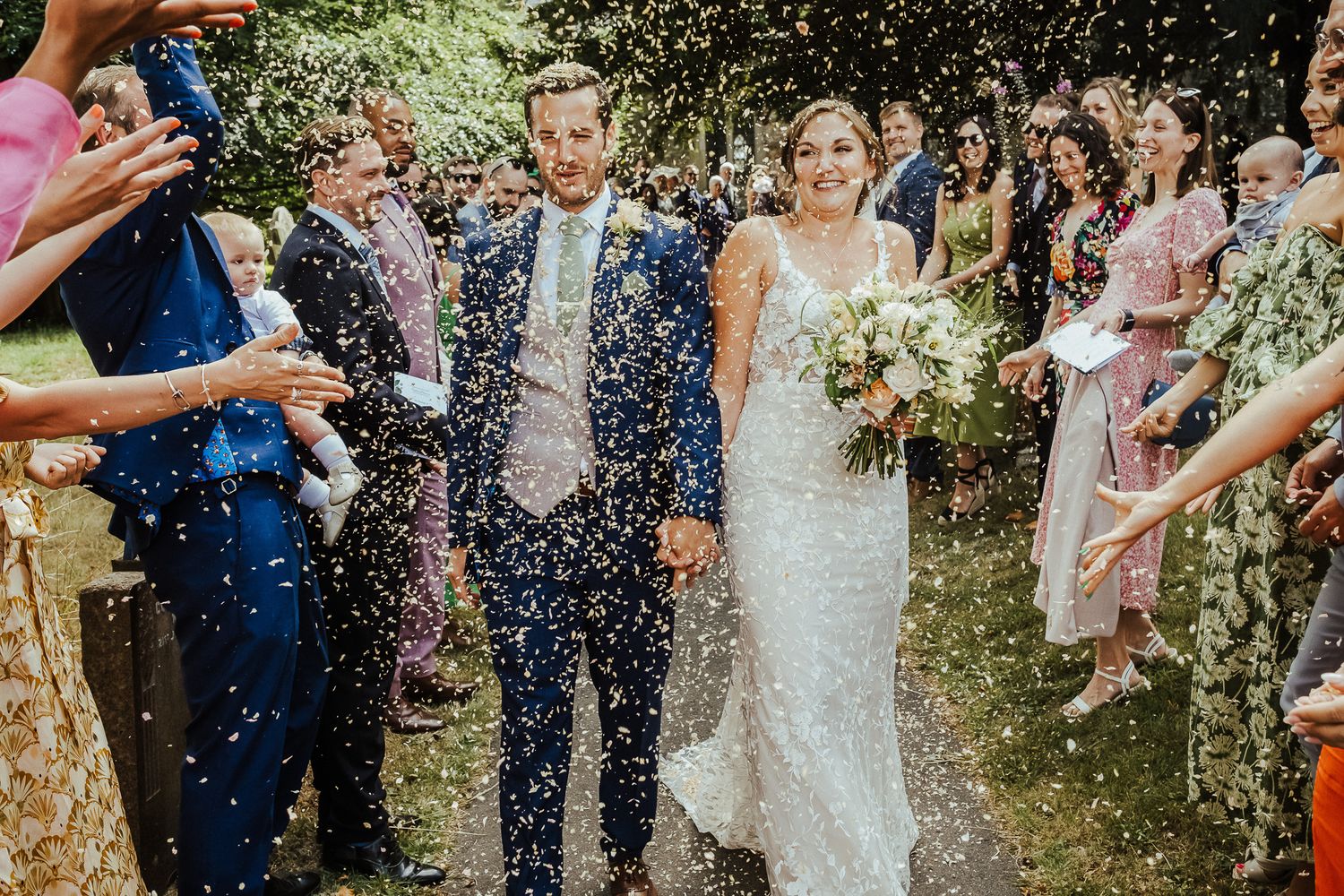 Newlyweds walking through shower of confetti surrounded by guests outdoors.