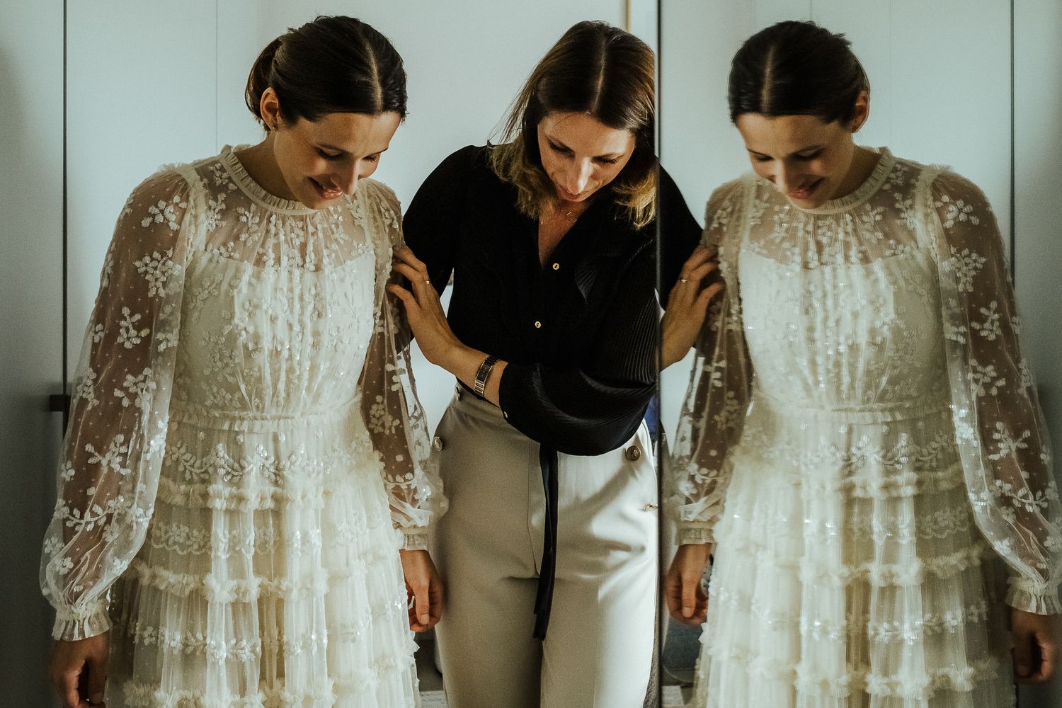 Two identical wedding dresses hanging beside stylist in black shirt.