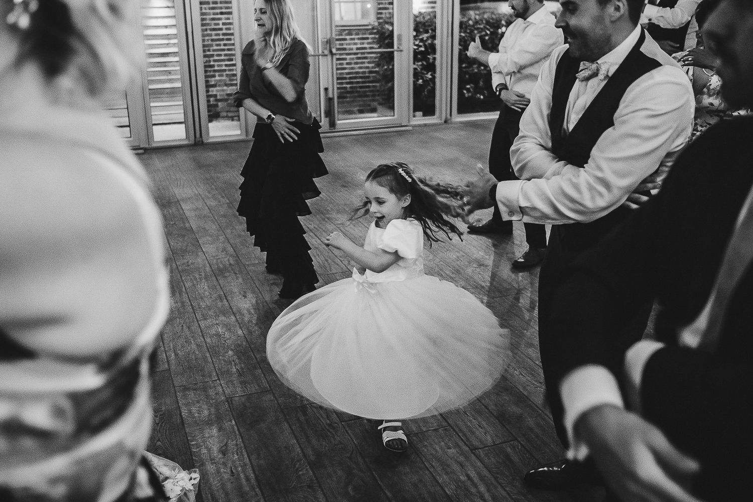Black and white photo of young girl in white dress twirling on dance floor.
