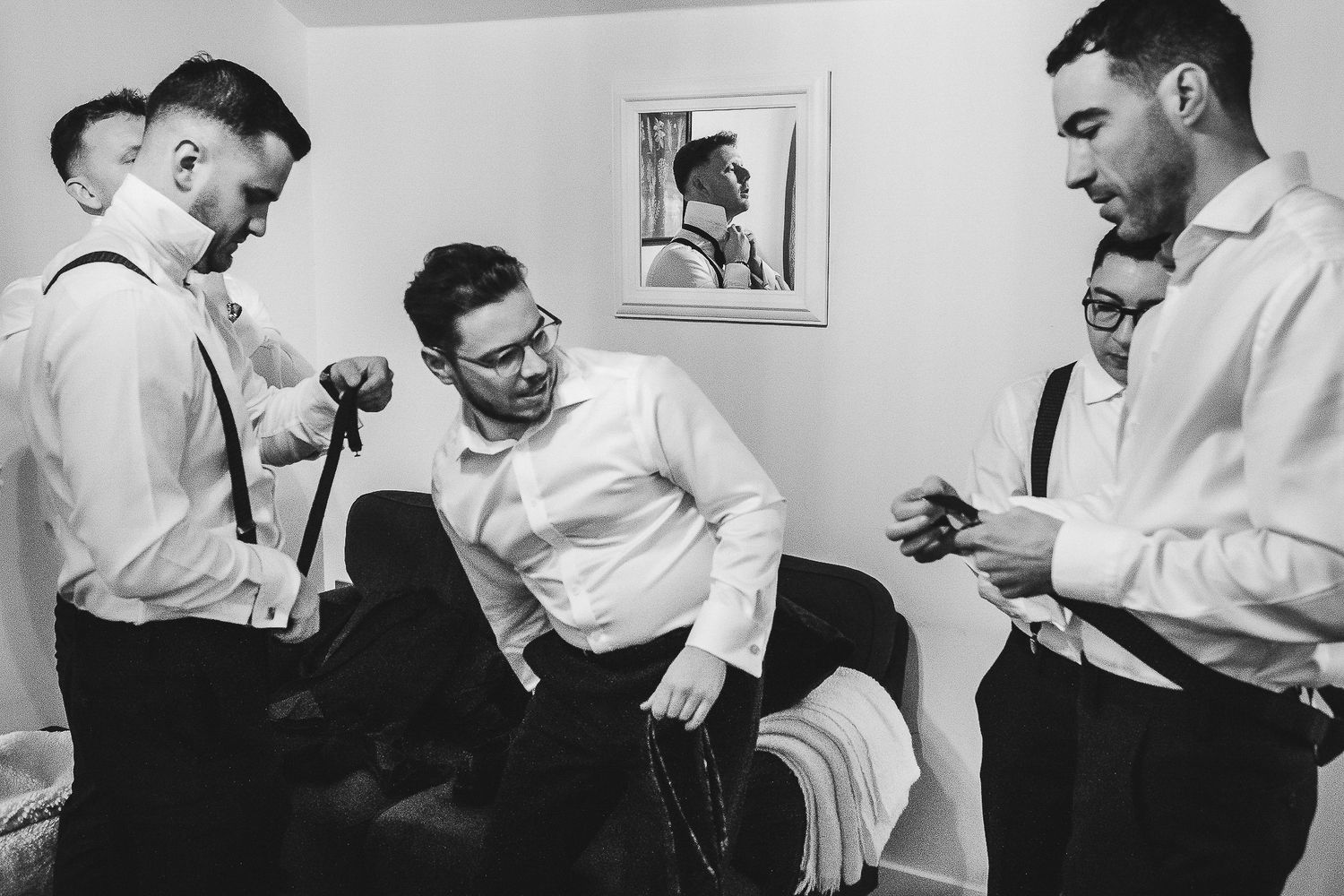 Groomsmen in white shirts laugh and get ready in black and white vintage photo.