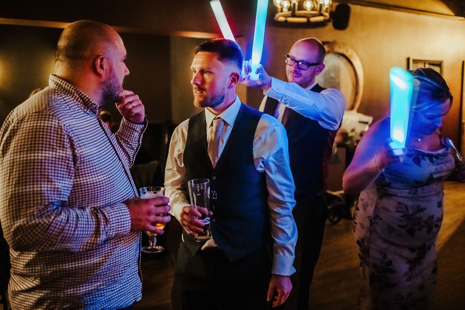 Wedding party members holding glowing blue lightsabers in dimly lit reception venue.